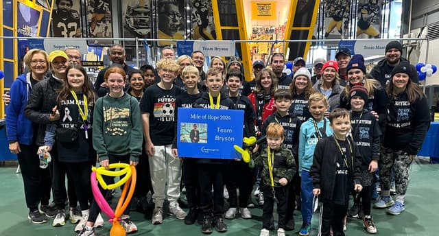 Team Bryson inside Acrisure Stadium holding a Mile of Hope 2024 sign, with balloon animals and the team banner behind them